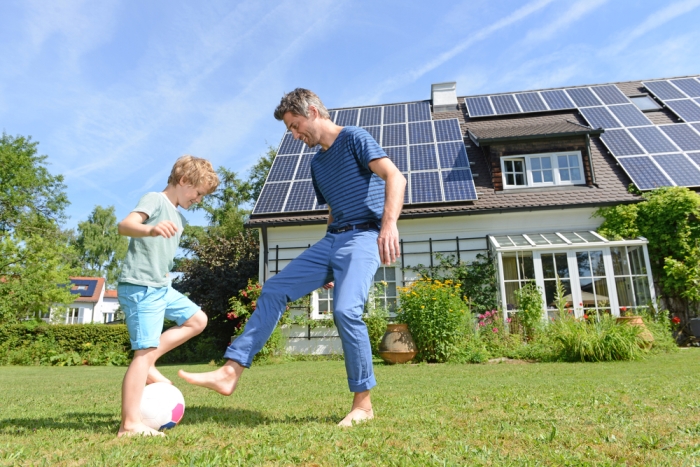 Father and son playing in yard of house with solar panels on roof